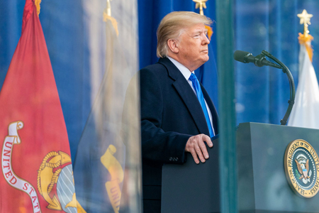 Pres. Donald Trump at a podium with presidential seal, U.S. Marine flags in background.